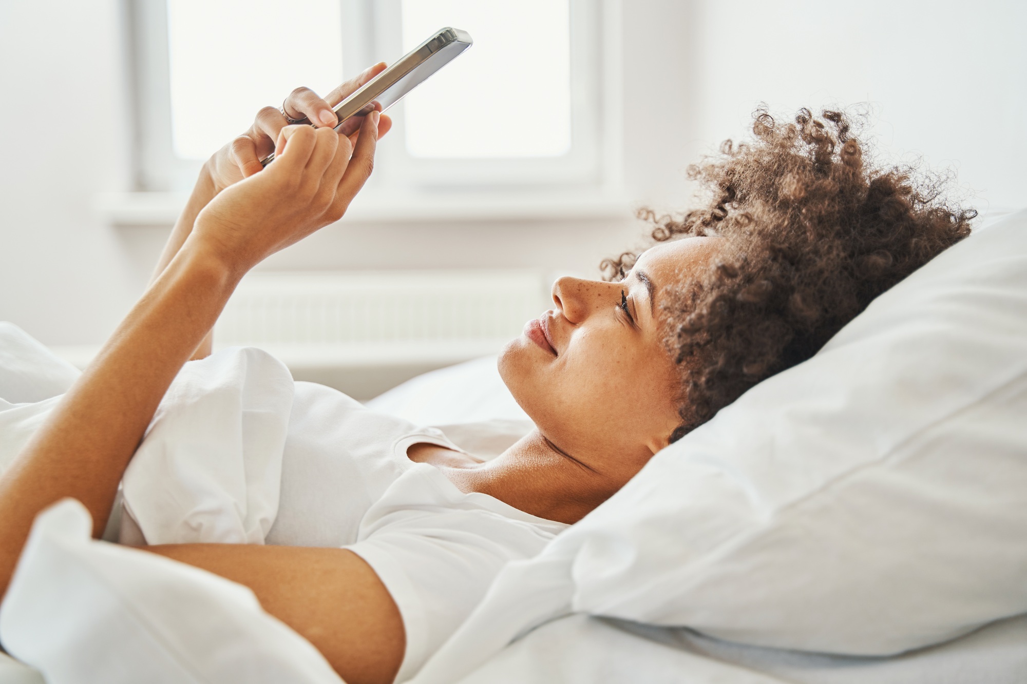 Smiling woman writing a text message in bed