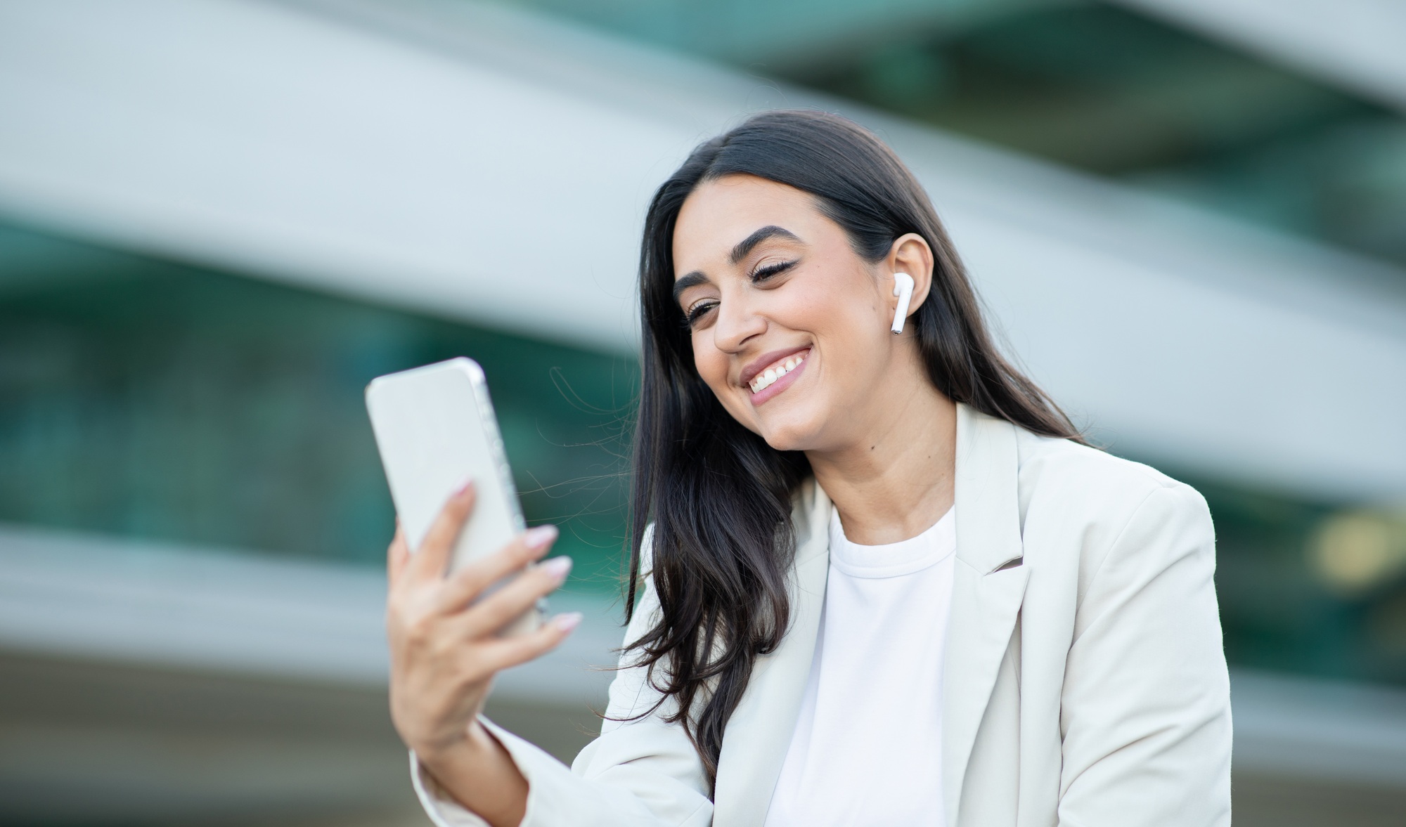 Smiling Woman Using Smartphone And Earbuds Outdoors