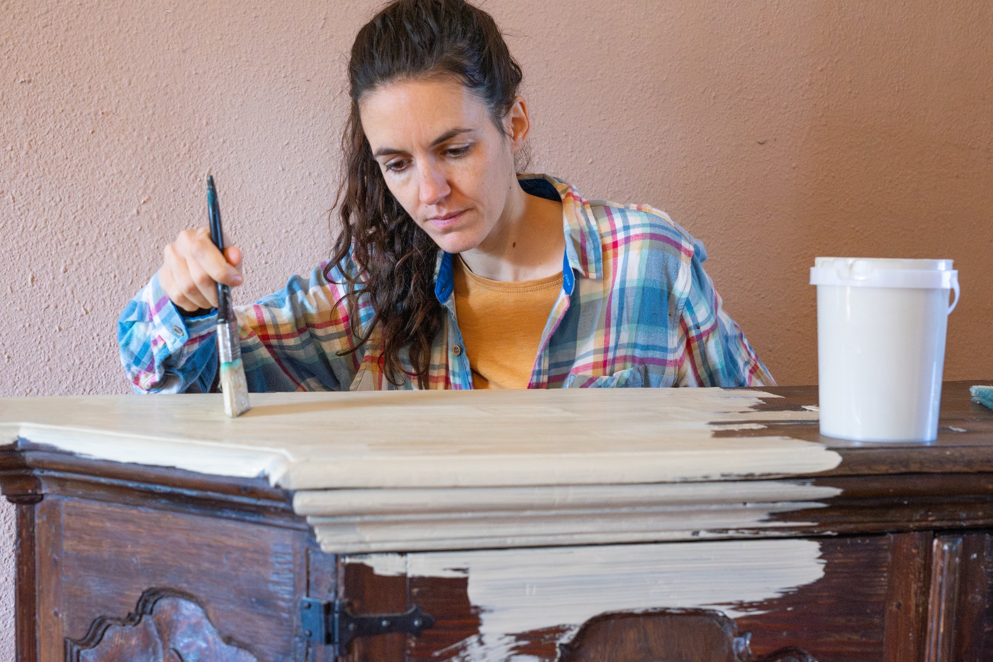 Woman restoring old furniture applying chalk paint with brush